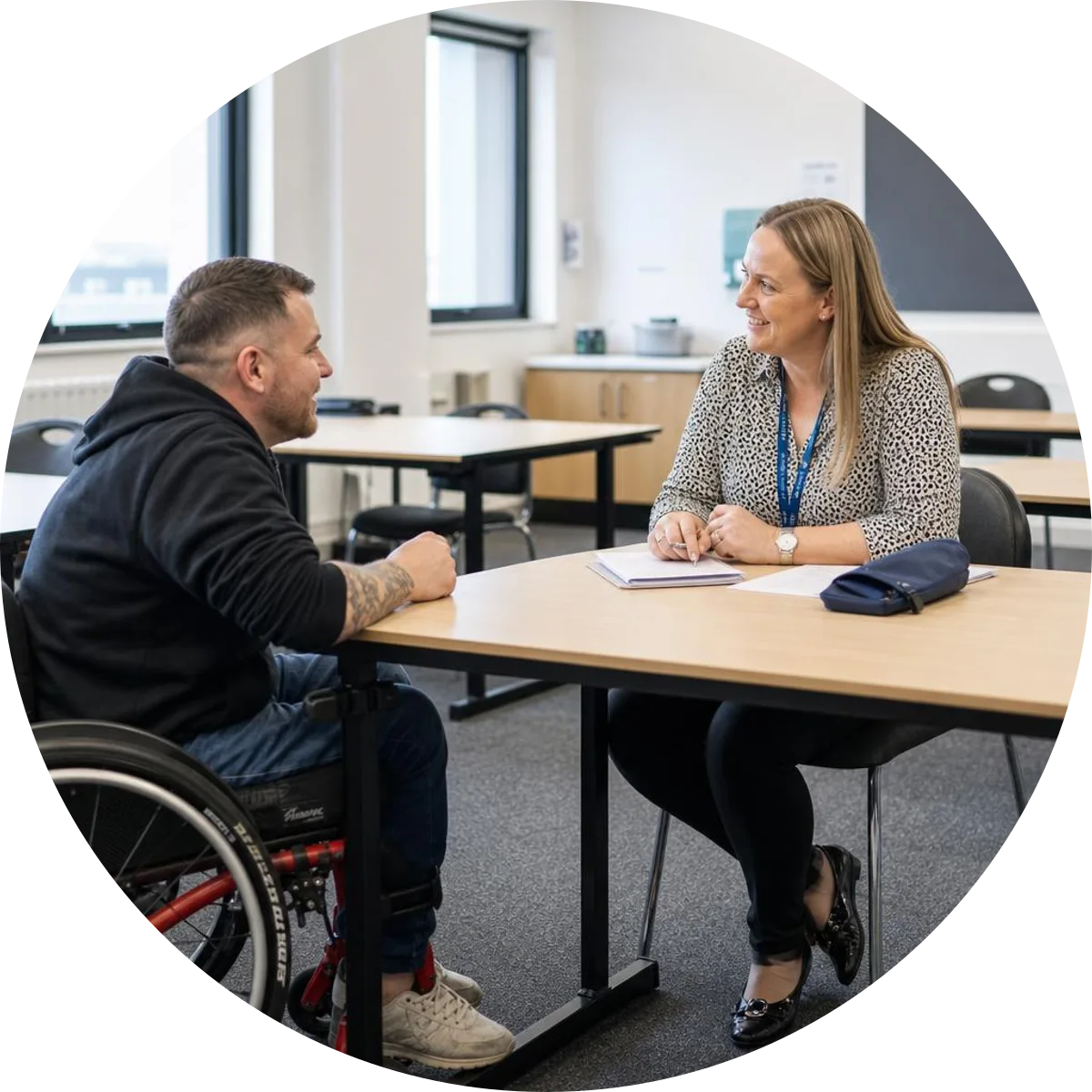 A wheelchair user discussing a course with an instructor beside a passive training manikin